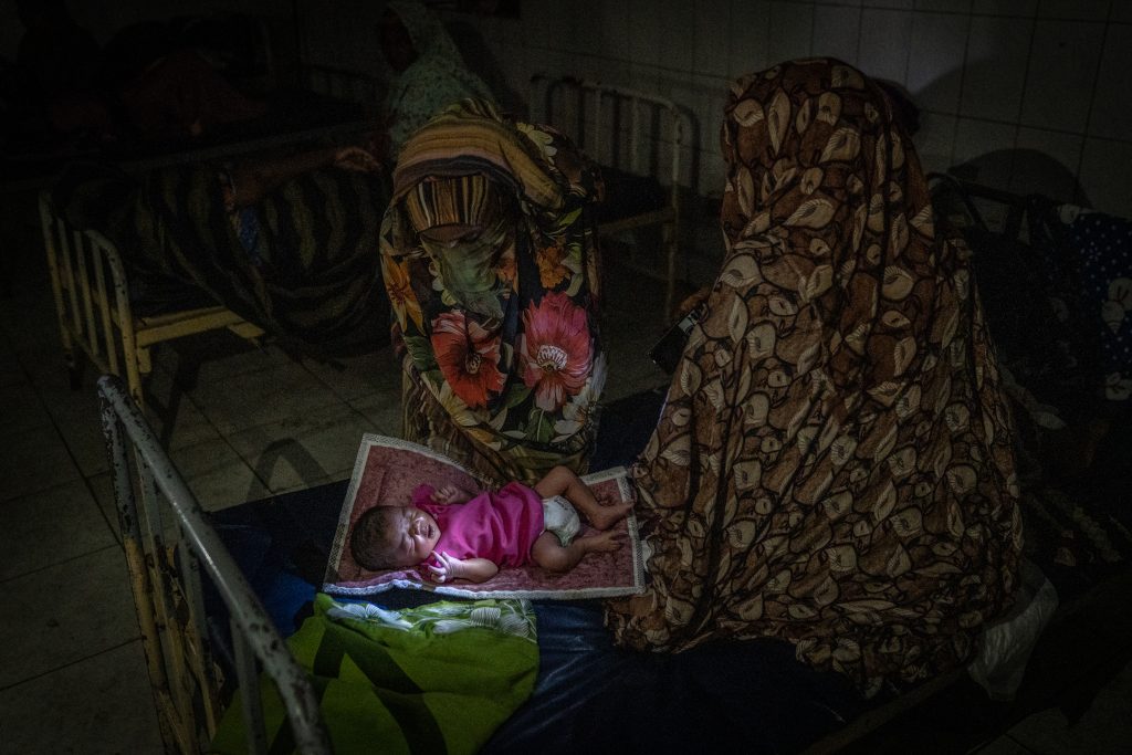 NEW HALFA HOSPITAL, NEW HALFA, SUDAN. January 18, 2025. A mother tends to her newborn baby, born just hours earlier, in a dimly lit maternity ward in New Halfa, 40 kilometers from Kassala in eastern Sudan. The hospital, which is managed by the Kassala State Ministry of Health and supported by UNFPA, was plunged into darkness on January 18th following a nearby drone attack on a hydroelectric power facility.